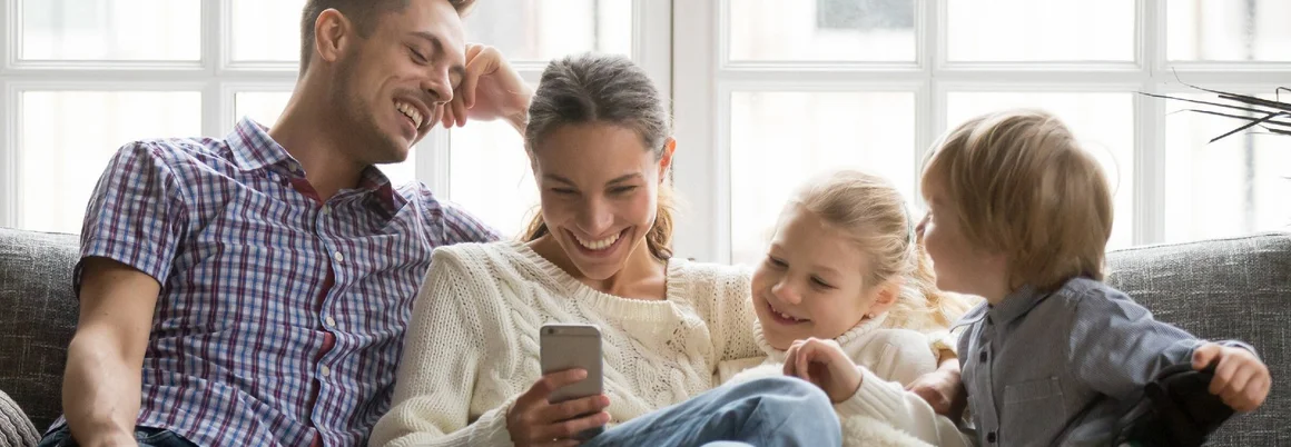 Eine Familie sitzt lachend gemeinsam auf dem Sofa